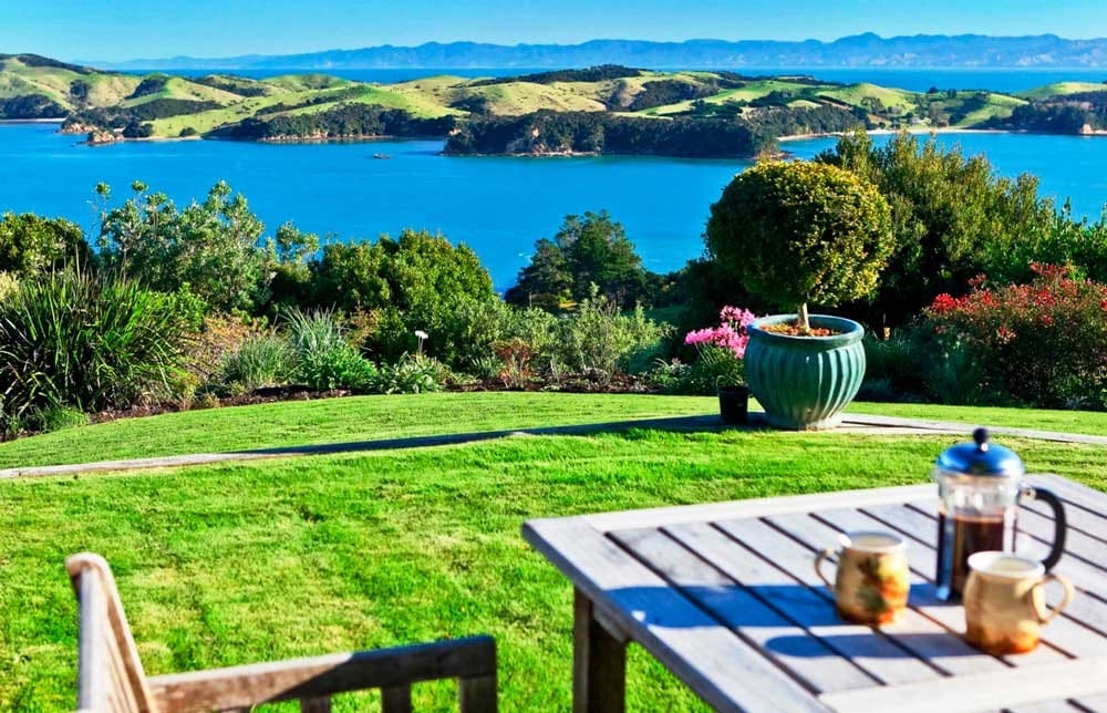 fotografía de una mesa de madera con una silla en el césped y de fondo vistas al mar y a las montañas